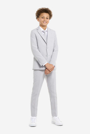In this image, a kid is wearing a formal grey suit. The suit consists of a blazer, pants and tie. Kids has two hands in front of suit.