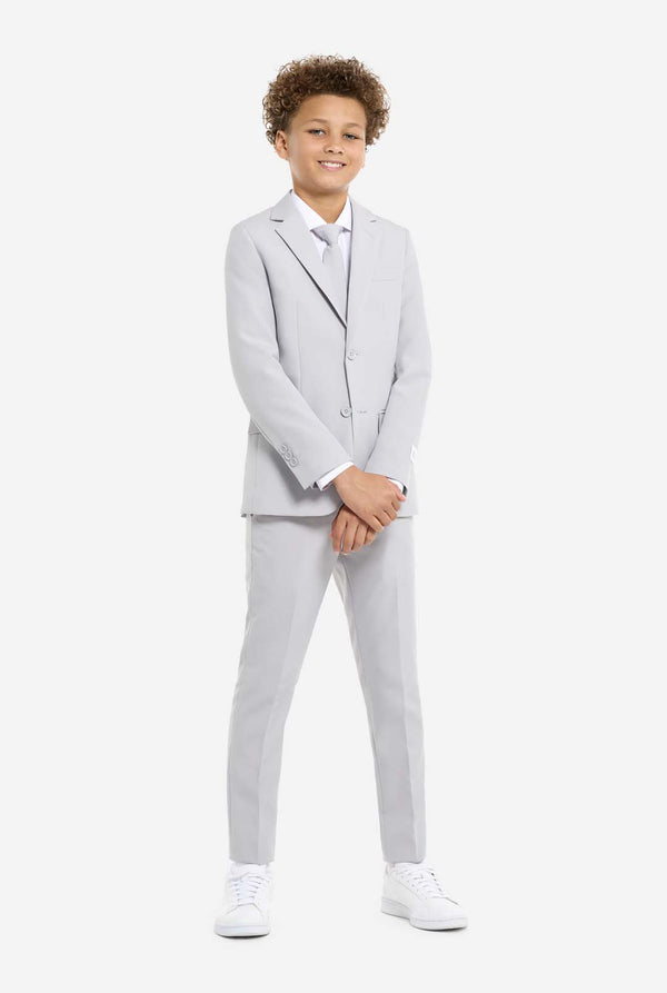 In this image, a kid is wearing a formal grey suit. The suit consists of a blazer, pants and tie. Kids has two hands in front of suit.