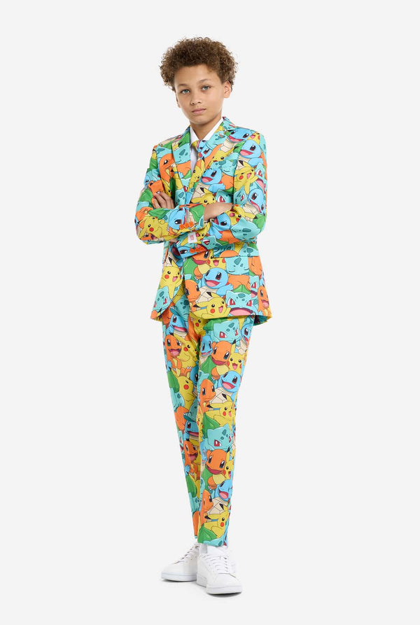 Teen wearing formal multi color suit with all-over Pokemon print. The suit contains the characters Pikachu, Bulbasaur, Charmander and Squirtle. Kid standing with crossed arms.