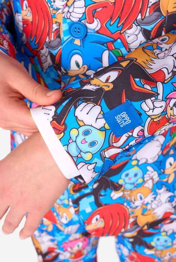 Teen boy wearing a vibrant Sonic teen suit featuring colorful prints of Sonic the Hedgehog characters including Sonic, Knuckles, Tails, and Amy, paired with a matching tie and white shirt. Sleeve close-up.