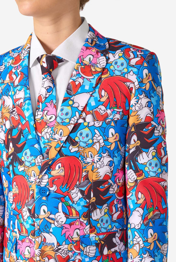 Teen boy wearing a vibrant Sonic teen suit featuring colorful prints of Sonic the Hedgehog characters including Sonic, Knuckles, Tails, and Amy, paired with a matching tie and white shirt. Close-up chest.