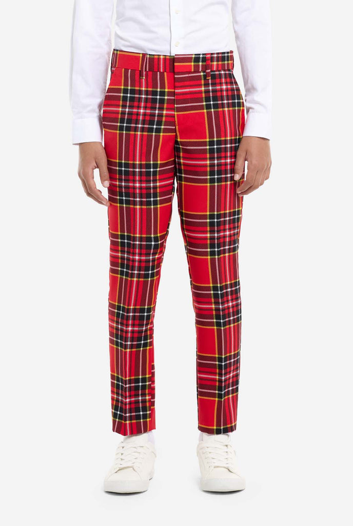 A young boy is wearing a stylish red plaid suit, known as The Lumberjack by OppoSuits. This teen boys' suit features a bold red, black, and yellow tartan pattern, perfect for holiday parties, formal events, or casual occasions that call for a playful yet classy look. The suit includes a matching jacket, trousers, and tie, all designed with a slim fit cut for a modern, youthful appearance. The boy pairs the suit with a crisp white shirt, enhancing the vibrant colors of the plaid pattern. Pants close up.