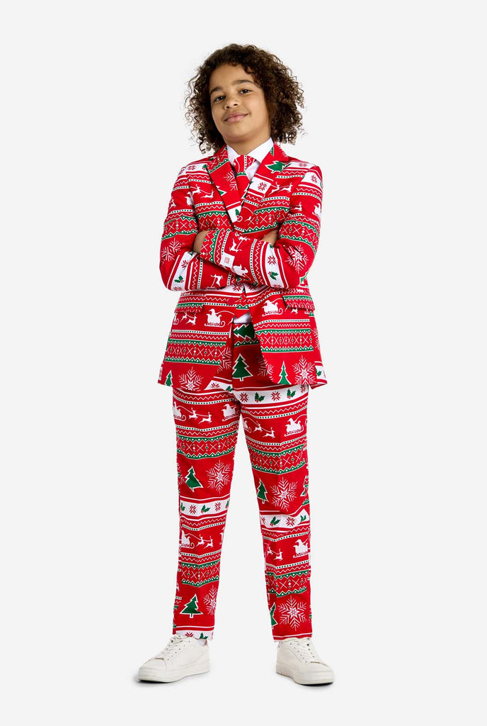 Teen wearing red Christmas suit with green and white Christmas icons, like Christmas tree, snowflakes, holly and sled with reindeers. Arms are crossed.