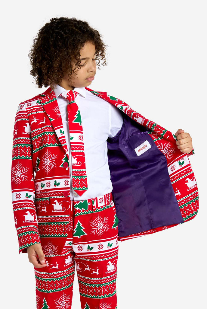 Teen wearing red Christmas suit with green and white Christmas icons, like Christmas tree, snowflakes, holly and sled with reindeers. Holding one side of the jacket open.