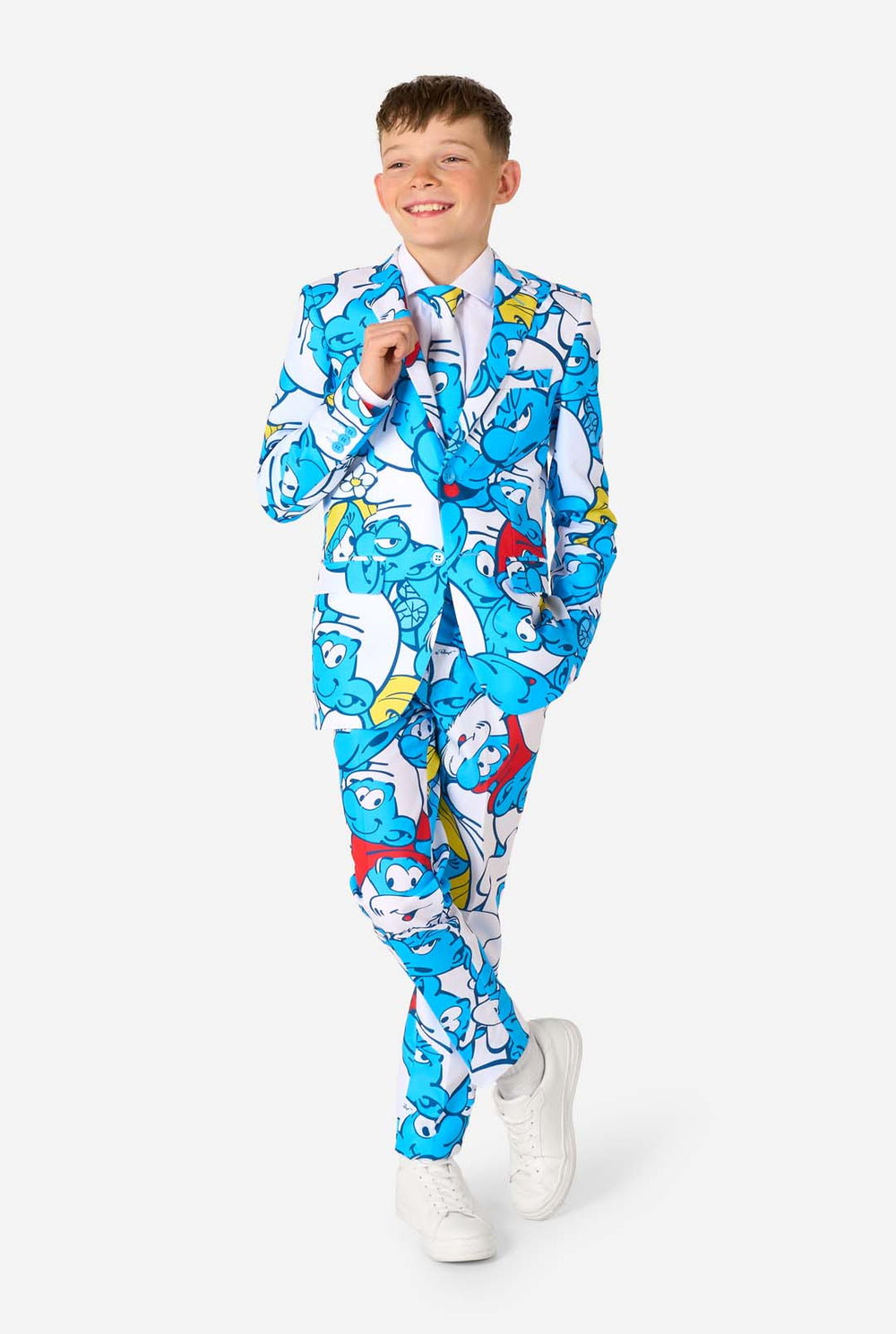 Teen boy wearing a vibrant Smurfs kids suit with colorful cartoon character prints in blue, red, yellow, and white, paired with a matching tie and white shirt, smiling against a plain background. 
