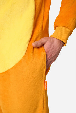 Close-up of a person wearing a fuzzy one-piece animal-style pajama or kigurumi in bright orange and pale yellow, with a hand inserted into a side pocket against a light gray background.