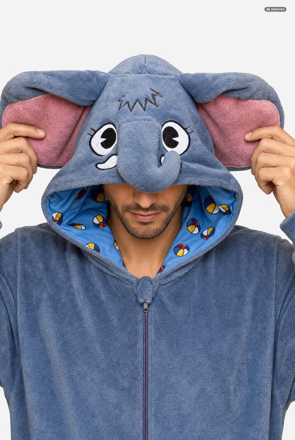 A man wearing a blue elephant-themed zip-up hooded onesie, holding the hood up to show the large floppy elephant ears with pink inner lining and a blue patterned interior.
