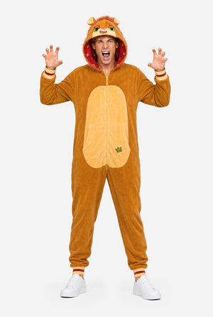 A man wearing a plush lion onesie pajama with a hood featuring a lion face and ears, a tan belly patch, and a red patterned hood lining, against a white background. Full body image.