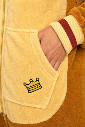 Close-up of a plush fleece one-piece garment in pale yellow, showing a hand in a front pocket with a small yellow crown embroidery and a cream-and-red striped cuff.