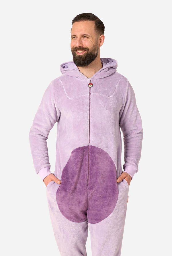 A man wearing a light purple full-zip hooded onesie with a darker purple oval patch on the front, standing against a plain light gray background.