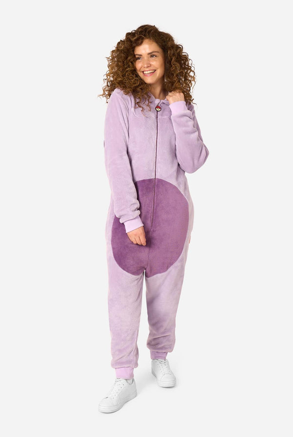 A woman modeling a lavender and purple animal-print onesie with white sneakers, standing against a light gray background.