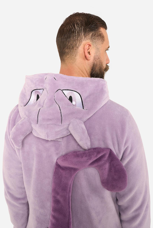 A man wearing a plush lavender-purple hooded onesie with a Mewtwo face on the hood and a matching curved tail detail on the back, shown from behind against a plain light background.