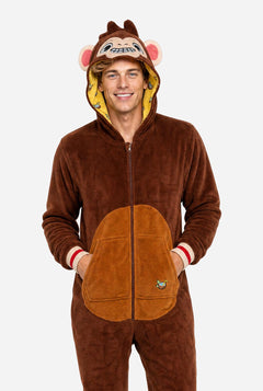 A man wearing a brown plush animal onesie with a hood shaped like a monkey face, featuring pink ears, a yellow inner hood lining, and a large tan belly patch on the front, photographed against a light gray studio background.