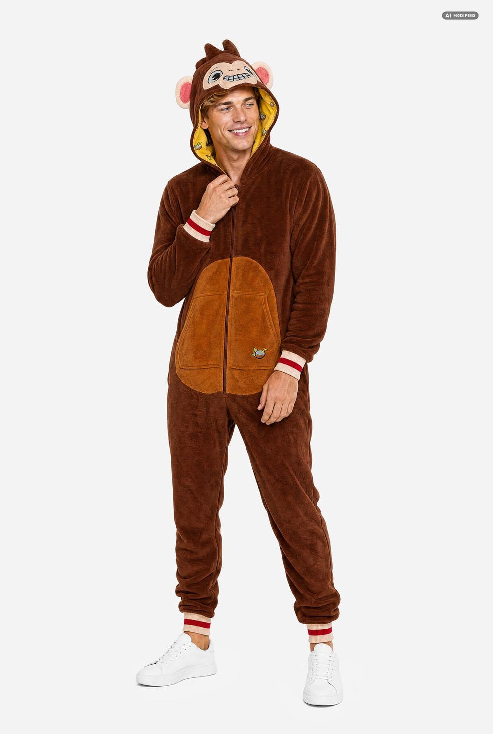 A man wearing a brown plush monkey onesie with a hood featuring a monkey face and pink ears, standing against a light gray background.
