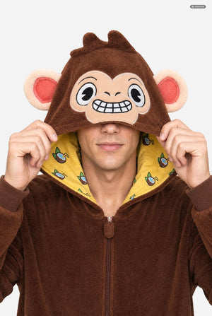 A man wearing a brown plush monkey hooded onesie, holding the hood up to show a cartoon monkey face with pink ears and a yellow patterned lining.