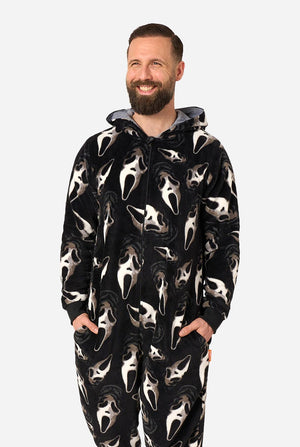 A smiling man with a beard wearing a black hooded one-piece pajama or kigurumi with an all-over Ghostface face print, posed against a light gray studio background.
