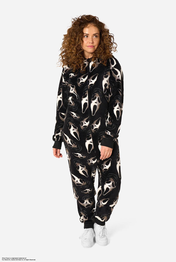A model with curly brown hair wearing a black hooded onesie with a white screaming face pattern, paired with white sneakers, against a light gray background.