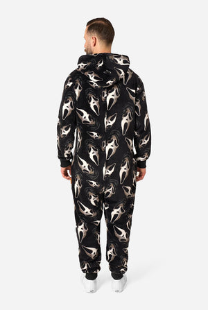 A man viewed from behind wearing a black hooded one-piece jumpsuit with an all-over shark face print in white and gray, paired with white sneakers, against a light gray studio background.