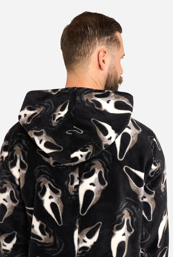 A man shown from the back wearing a plush hooded sweatshirt with an all-over Ghostface-style print in black, white, and gray on a light gray studio background.