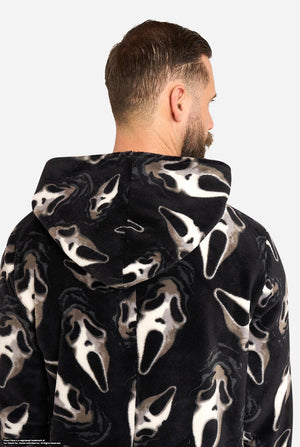 A man modeling black hooded onesie or junpsuit with an all-over white Ghost Face print, standing against a light gray studio background. Close-up from the back.