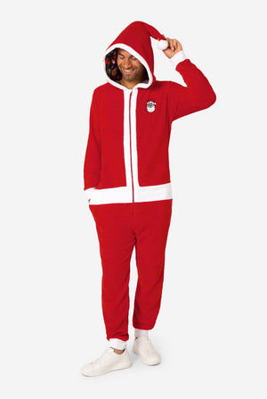 A smiling man models a cozy, red and white, hooded christmas onesie that resembles a Santa onesie. Full body image