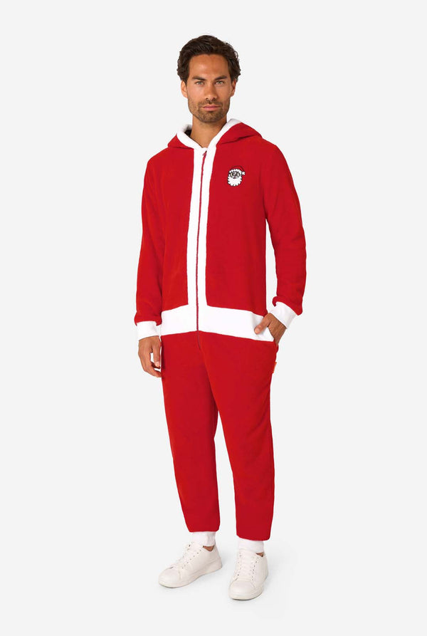 A smiling man models a cozy, red and white, hooded christmas onesie that resembles a Santa onesie. Full body image