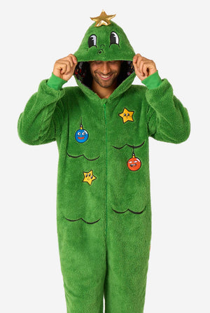 A smiling man wearing a green Christmas onesie designed to look like a Christmas tree, decorated with cartoon ornaments and stars. Hood on it's head