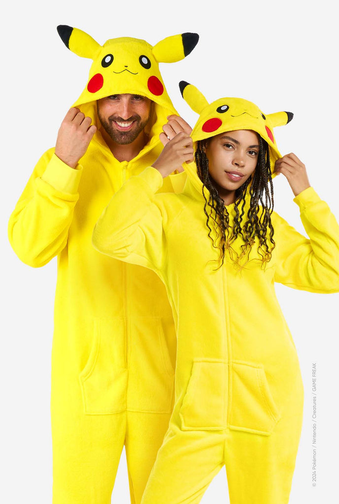 A man and woman are wearing a vibrant Pikachu onesie, designed to resemble the iconic Pokémon character. This unisex adult onesie is bright yellow with Pikachu’s recognizable face on the hood, featuring large black-tipped ears, black eyes, red cheeks, and a cute smile. The onesie has a convenient front zipper closure and two front pockets for functionality and comfort. The soft, cozy material makes it perfect for lounging, cosplay events, or Pokémon-themed gatherings. Ideal for Pokémon fans.