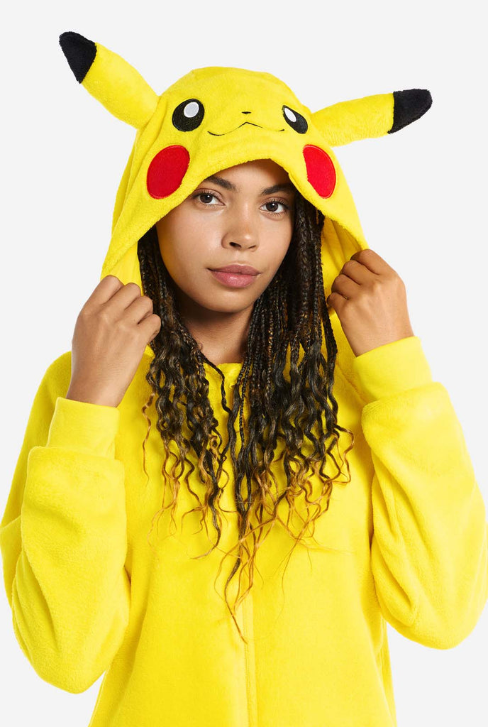 A woman is wearing a vibrant Pikachu onesie, designed to resemble the iconic Pokémon character. This unisex adult onesie is bright yellow with Pikachu’s recognizable face on the hood, featuring large black-tipped ears, black eyes, red cheeks, and a cute smile. The onesie has a convenient front zipper closure and two front pockets for functionality and comfort. The soft, cozy material makes it perfect for lounging, cosplay events, or Pokémon-themed gatherings. Ideal for Pokémon fans. Close up.