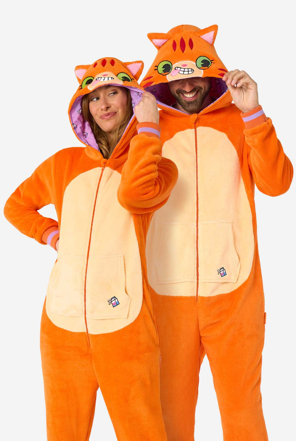 A man and women are wearing an orange adult onesie designed as a red cat onesie. The onesie features a hood resembling a cat's head, and cat details, perfect for cozy lounging or costume parties. Both have the hood on their head.