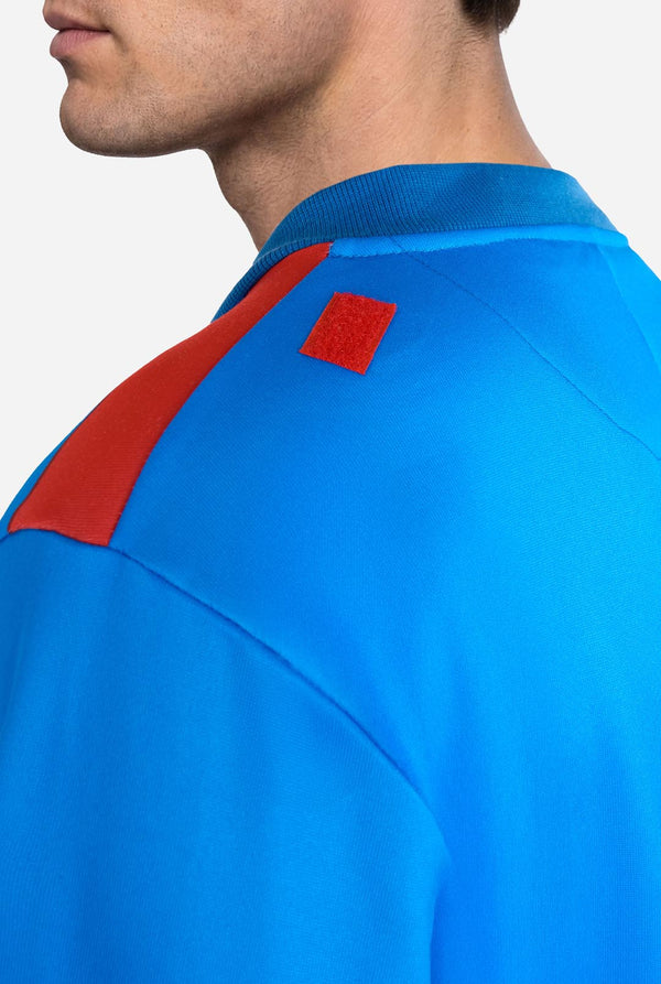 Image of a man wearing a blue and red Superman onesie with a red cape on a light background. Close up back.
