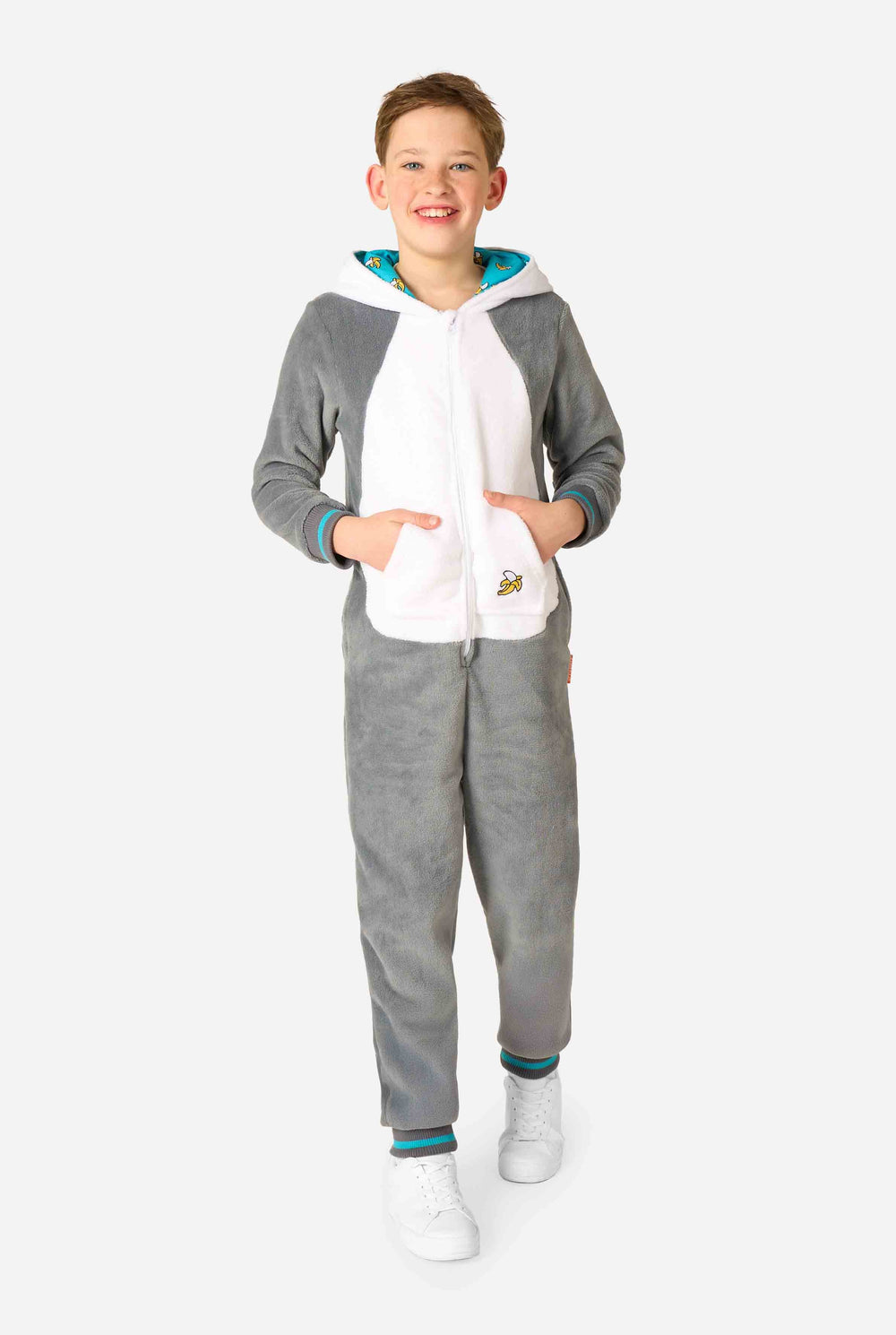 Child wearing a cozy unisex kids onesie designed as a lemur, featuring grey and white plush fabric, a hood with a cartoon lemur face and ears, and a playful banana print on the pocket.
