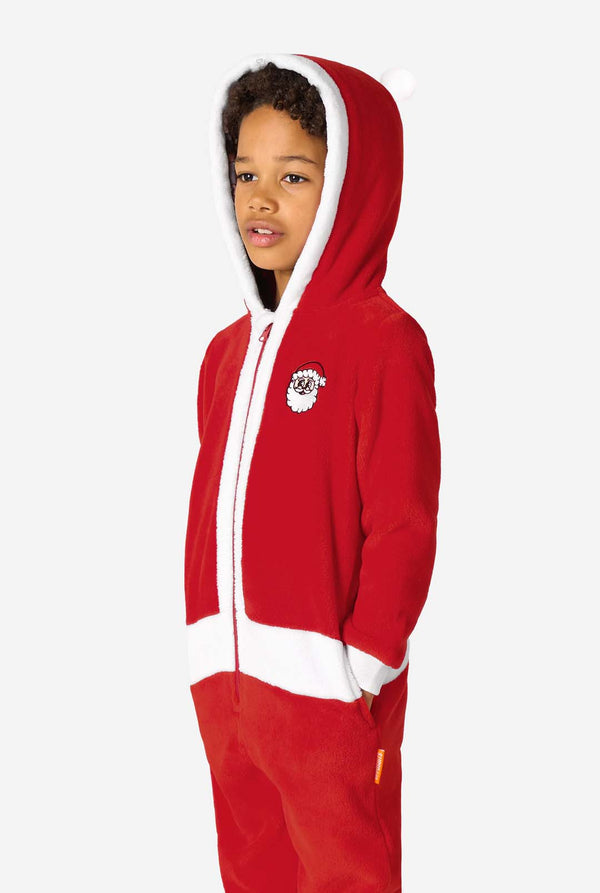 Child wearing a red Santa-themed onesie with a white-trimmed hood, standing angled to the side with hands in the pockets.