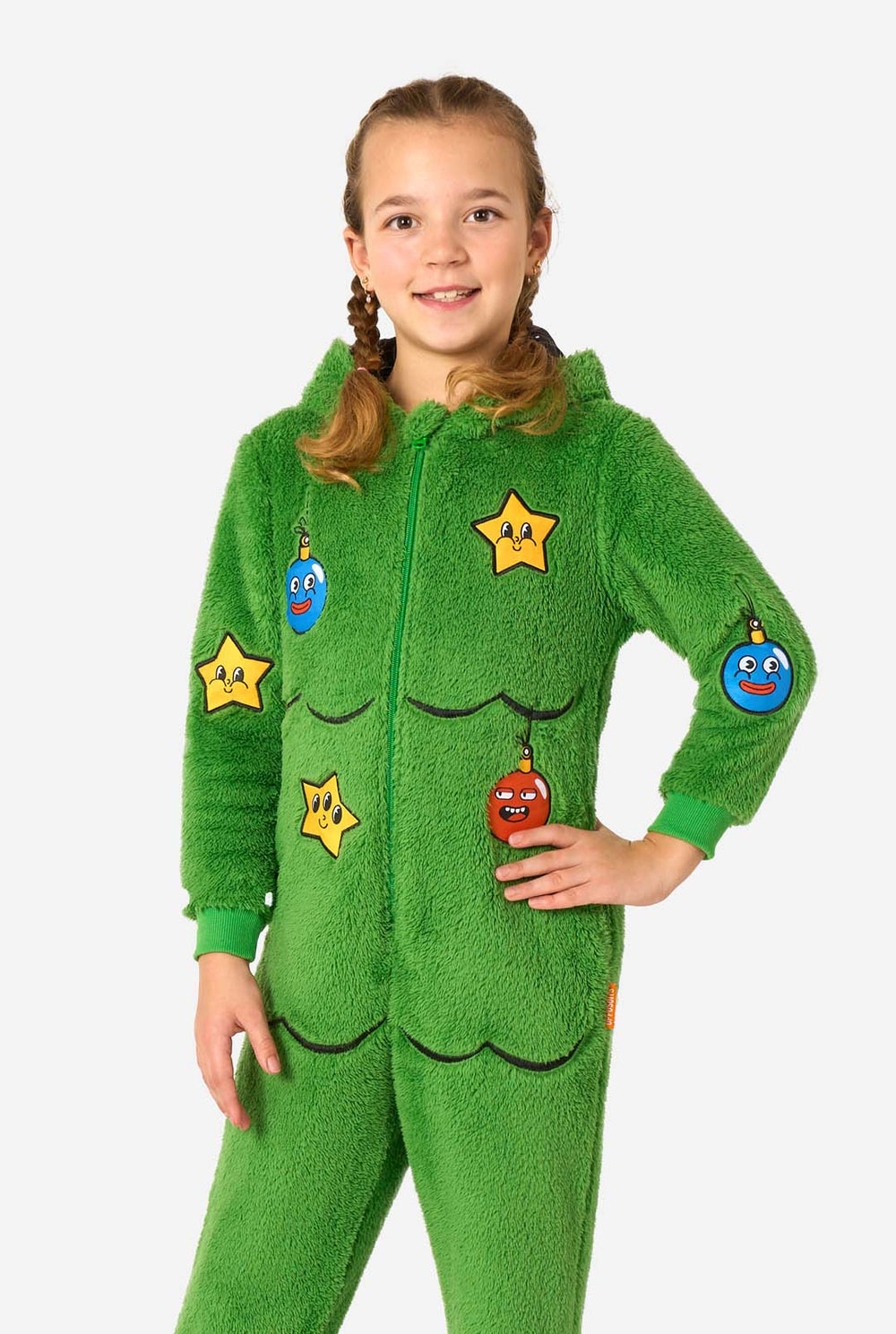 Child wearing a green Christmas tree–shaped onesie with a hood featuring cartoon eyes and a gold star on top, holding the hood.