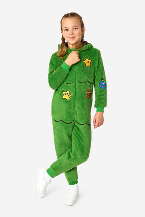 Child standing with one leg bent, wearing a green Christmas tree onesie with cartoon ornaments and a zip front.