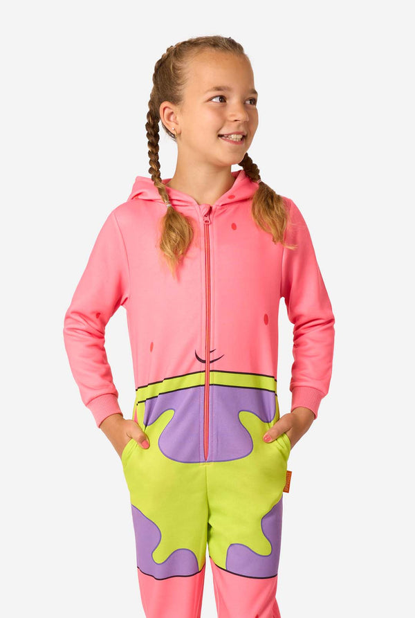 Child wearing a pink Patrick Star onesie with purple-and-neon green shorts print, standing with hands in the pockets and smiling to the side.
