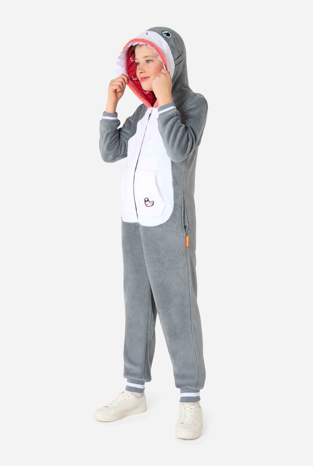 A kid is wearing a grey and white shark kids onesie featuring playful hood details and cozy, soft material, perfect for lounging or costume events. 