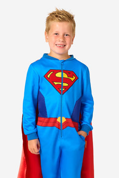 Child wearing a Superman-themed onesie with a red cape on a white background