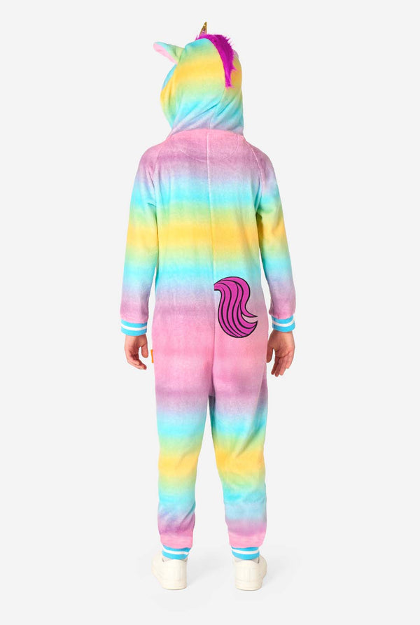 A smiling kid is wearing a white, pink, blue and yellow kids onesie designed as a unicorn. The Unicorn onesie features a hood resembling a unicorn head and other playfull details. View from the back, full body.
