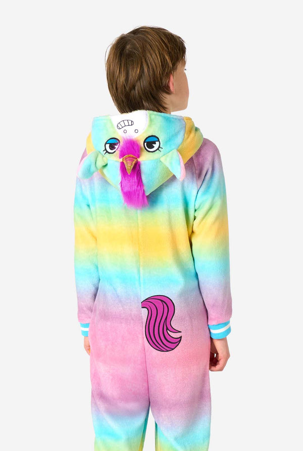 A smiling kid is wearing a white, pink, blue and yellow kids onesie designed as a unicorn. The Unicorn onesie features a hood resembling a unicorn head and other playfull details. View from the back.