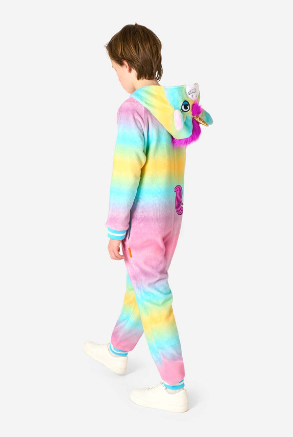 A smiling kid is wearing a white, pink, blue and yellow kids onesie designed as a unicorn. The Unicorn onesie features a hood resembling a unicorn head and other playfull details, View from the back with the hood down.