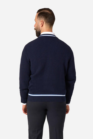 A man viewed from the back wearing a navy blue ribbed knit sweater with white stripes at the collar and hem, paired with dark trousers, against a light gray studio background.