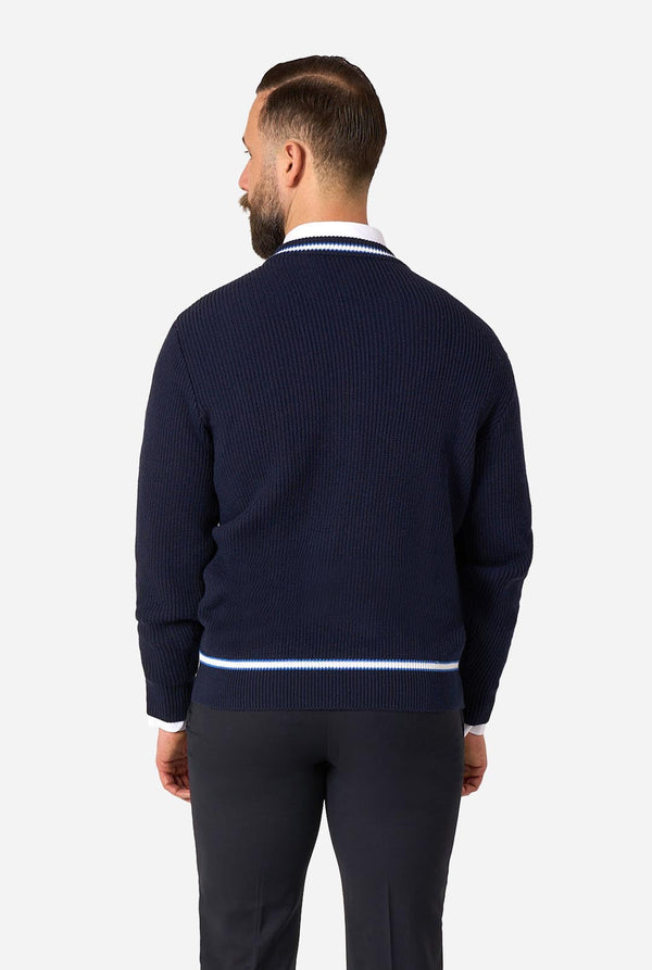 A man viewed from the back wearing a navy blue ribbed knit sweater with white stripes at the collar and hem, paired with dark trousers, against a light gray studio background.