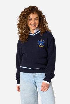 A woman with curly brown hair wearing a navy blue knitted sweater with a Harry Potter Ravenclaw crest on the chest, styled with light blue jeans against a plain white background.