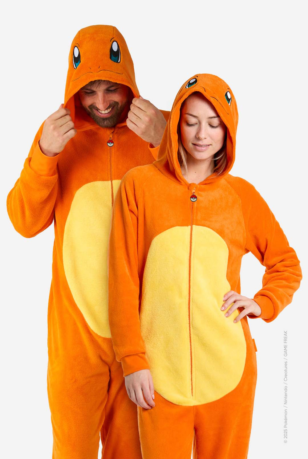 Two people wearing matching orange and yellow Pokémon Charmander onesies on a grey background