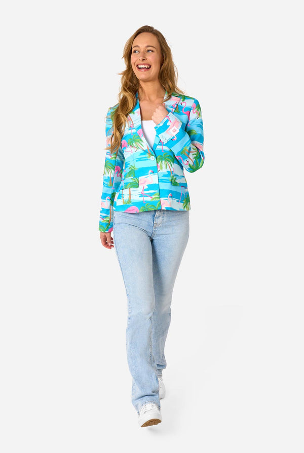 Image with a light background and a woman wearing a light blue blazer with tropical flamingo print and jeans. Full body image.