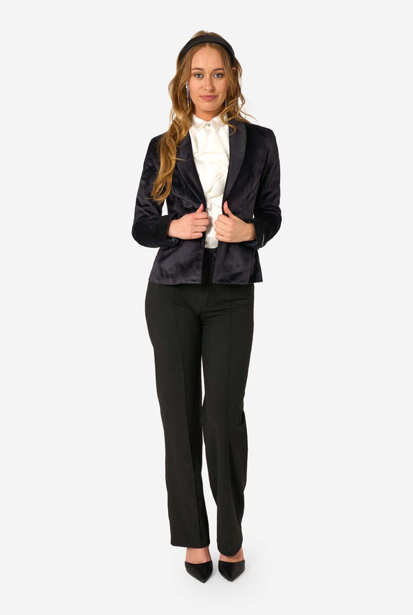 Woman wearing a black velvet blazer, black pants, and a white shirt on a white background