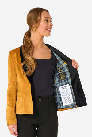 Woman wearing a velvet golden blazer with black lapels on a white background, opening one side of the jacket.
