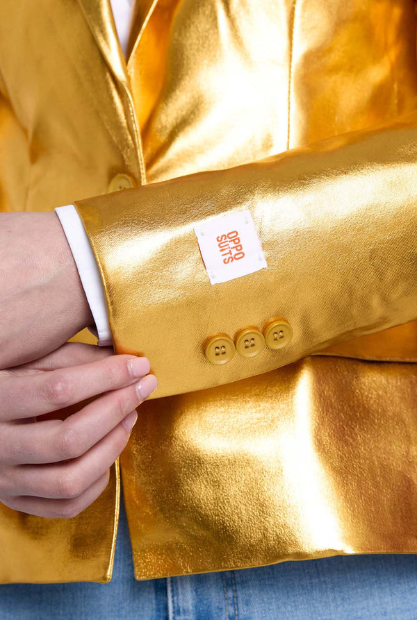 Gold jacket with a brand label being held by a person wearing blue jeans.