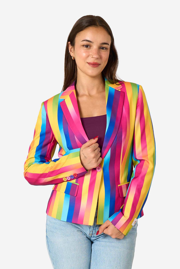 Woman wearing a colorful rainbow striped blazer and light blue jeans against a white background.
